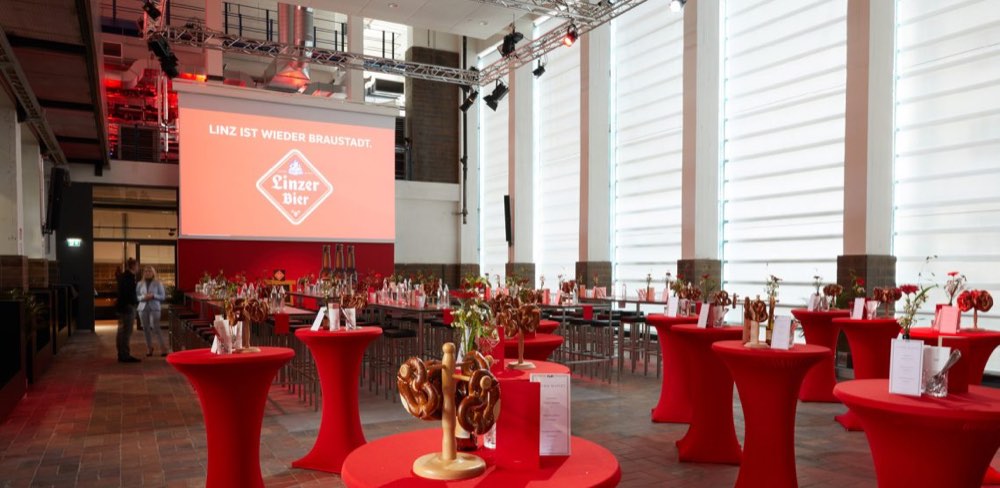 Hörsaal 0 mit Stehtischen und Leinwand vor der hohen Fensterfront des Kraftwerks